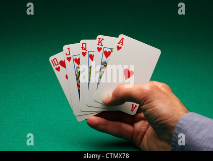 Una mano d'uomo azienda carte da gioco su un tavolo verde. Un Royal Flush di cuori nel gioco del Poker Foto Stock