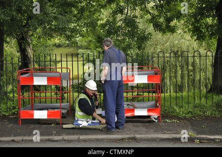 British Telecom engineer lavorando su apparecchiature sotterraneo con barriere di avvertimento pericolo in posizione con il collega cercando su Foto Stock