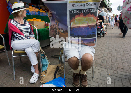 Lettore del Daily Telegraph newspaper legge circa la notte precedente Olympic cerimonia di apertura, il primo giorno di gara del London 2012 Olympic 250km mens' la gara su strada. A partire da Londra centrale e passando la capitale più famosi luoghi di interesse prima di uscire in Inghilterra rurale all'estenuante Box Hill nella contea del Surrey. Sud-ovest locali londinesi rivestito il percorso sperando per preferito britannico Mark Cavendish per vincere Team GB prima medaglia ma che sono poi stati delusi quando il Kazakistan è Alexandre Vinokourov alla fine ha vinto l'oro. Foto Stock