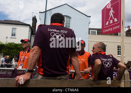 Olympic i volontari attendono l arrivo del ciclismo su strada concorrenti per la prima giornata di gara del London 2012 Olympic 250km mens' la gara su strada. Londra 2012 volontari sono chiamati 'Giochi Makers', come stanno contribuendo a rendere i giochi accadere. Fino a 70.000 giochi politici prendere su di una ampia varietà di ruoli attraverso le sedi: da accogliere i visitatori, per il trasporto di atleti; ad aiutare dietro le quinte nella tecnologia team per assicurarsi che i risultati visualizzare quanto più rapidamente e accuratamente possibile. Giochi politici provengono da una gamma diversificata di comunità e gli sfondi da tutto il Regno Unito. Foto Stock