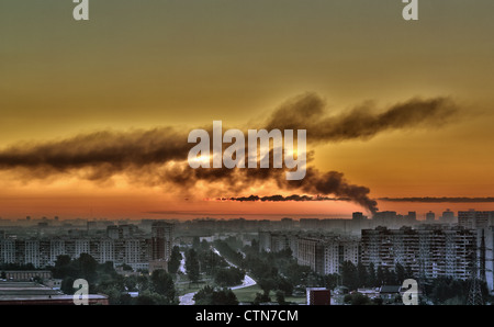 Il nero fumo di un incendio sullo sfondo di un orange sunrise in città Foto Stock