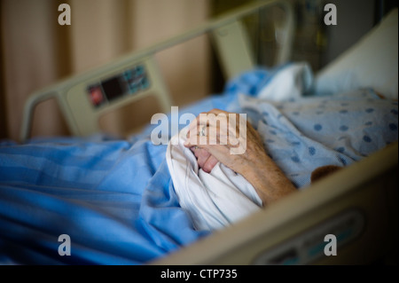 Vecchia donna con le mani in mano nel letto di ospedale. Foto Stock