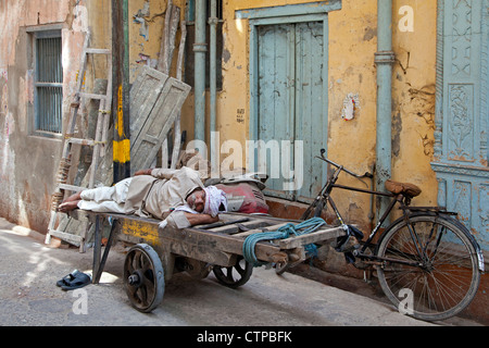 Il vecchio uomo dorme sul carrello di legno in strada nella Vecchia Delhi, India Foto Stock