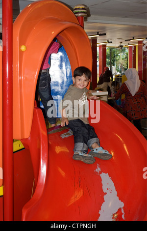 Giovane ragazzo di razza mista giocando su rosso luminoso scorrono in mcdonalds malang java indonesia Foto Stock