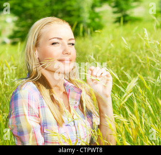 Carina ragazza bionda sul campo di grano, donna seduta su erba verde, femmina rilassante all'aperto, felice Pretty girl teen tenendo la segala Foto Stock