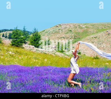 Bella ragazza che danzano sul campo di lavanda, cute teen in esecuzione sul fiore viola prato, bella donna gioca con sciarpa bianco Foto Stock