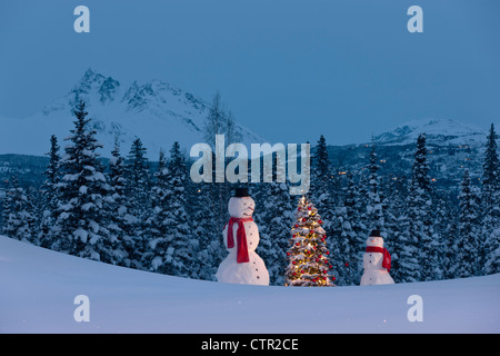 Foto adulto bambino pupazzi di neve che indossa foulard rosso nero in alto cappelli in piedi accanto albero di Natale illuminato rosso snowcovered ornamenti abete rosso Foto Stock