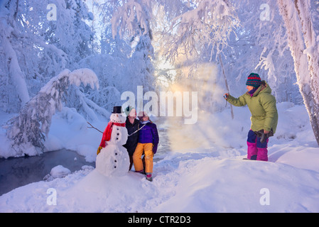Fotografie di madre marito figlia in posa accanto pupazzo di neve nel gelo coperta di foresta Jack russo molle di ancoraggio del Parco Foto Stock