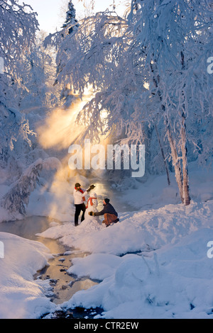 Marito e moglie la costruzione di pupazzo di neve in frosty forest retroilluminati da raggi solari del Jack russo Springs Park centromeridionale Alaska inverno Foto Stock