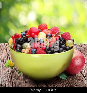 Ciotola con una varietà di frutti di bosco sul vecchio tavolo in legno. Contro lo sfondo di fogliame di estate. Foto Stock