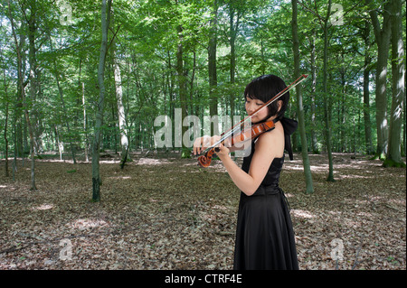 Femmina violinista asiatica a suonare il violino in foresta Foto Stock