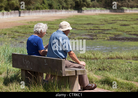 Anziani l uomo e la donna si sedette sul banco nella sunshine a Langston harbour a bassa marea con I love you grafitti Foto Stock