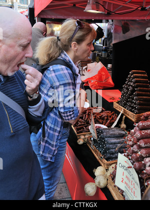 Una signora acquista salsicce provenienti da un mercato in stallo mentre un uomo campioni il chorizo. Foto Stock