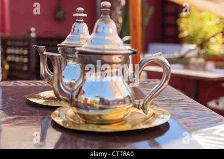 Due d'argento teiere immessi sul loro piastre essendo focalizzata più lontano in una di Marrakesh ristorante (Marocco) Foto Stock