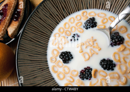 Ciotola di cereale con more e lettera pezzi sagomati l'ortografia delle parole imposta giorno galleggianti in un latte. Foto Stock