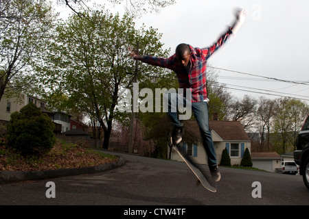 Un guidatore di skateboard esegue salti o ollies su asfalto. Una leggera sfocatura che mostra il movimento sulle braccia e sulle gambe. Foto Stock