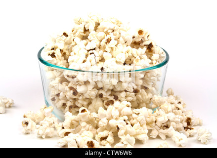 Cumulo di pop-corn che tracima da una chiara ciotola di vetro isolato su sfondo bianco con copia spazio. Foto Stock