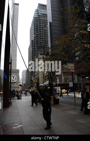 Ritratto di mattina, verso la settima Avenue, l'uomo con la spatola telescopico pulizia facciata in marmo Chase Bank, West 52nd Street, New York Foto Stock