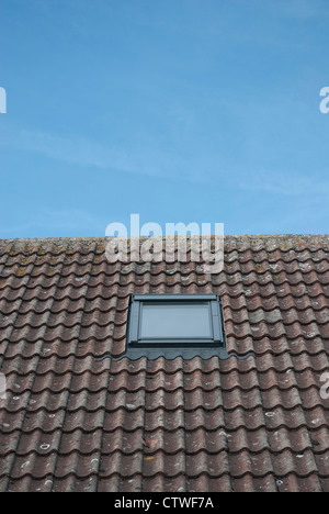 A Velux lucernario finestra in un tetto di tegole contro un luminoso cielo blu Foto Stock