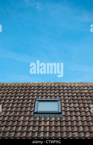 A Velux lucernario finestra in un tetto di tegole contro un luminoso cielo blu Foto Stock
