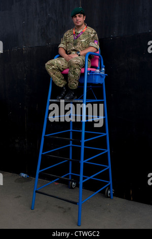 Un soldato Britannico dei Royal Marines si siede in un creatore di giochi di alta sedia per supervisionare un ingresso al Parco Olimpico durante le Olimpiadi di Londra 2012. Questa terra è stata trasformata in un 2.5 sq km complesso sportivo, una volta che le imprese industriali ed ora sede di otto luoghi di interesse tra cui il principale arena, Aquatics Centre e Velodromo plus degli atleti del Villaggio Olimpico. Dopo le Olimpiadi, il parco è noto come Queen Elizabeth Olympic Park. Foto Stock