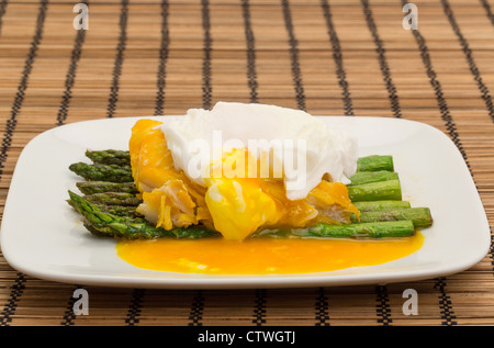 Eglefino affumicato, asparagi e un uovo in camicia la cena disposti su una piastra di Cina con il tuorlo svuotamento dall'Uovo affogato Foto Stock