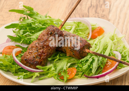 Carni bovine shish kebab o kofta con dolce condimento al peperoncino e prezzemolo e servite su un letto di insalata - studio shot Foto Stock