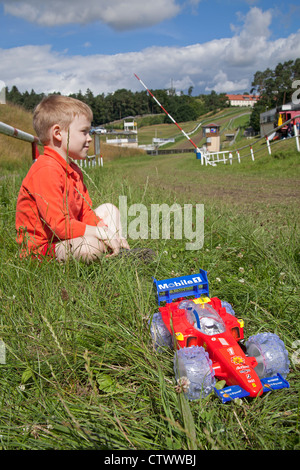 Ragazzo con il giocattolo auto racing seduti di fronte racetrack, Teterow, Mecklenburg-Switzerland, Meclemburgo-Pomerania Occidentale, Germania Foto Stock