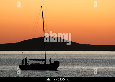 Silhouette di un yacht contro un tramonto rosso con acqua riflettente Foto Stock