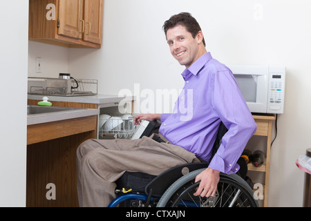 Uomo in carrozzella con lesioni del midollo spinale di mettere i piatti in una lavastoviglie accessibile Foto Stock