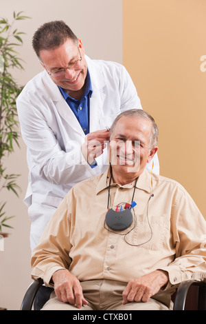 Regolazione Audiologist dietro l'orecchio udito un aiuto in un orecchio del paziente durante la programmazione Foto Stock