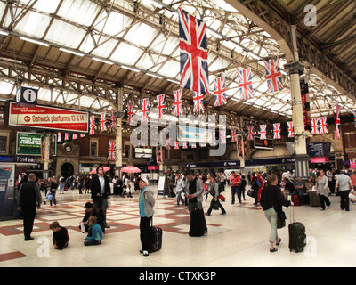 Passeggeri attendere all'interno della stazione ferroviaria di Victoria con Union Jack appesa sopra durante il 2012 Giochi Olimpici ospitati da Londra Foto Stock