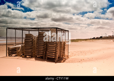 Sedie a sdraio impilati e recintata su una spiaggia deserta Foto Stock