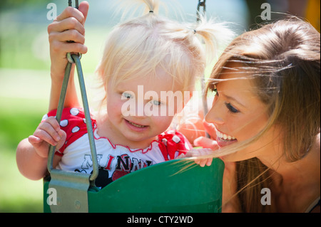 Giovane madre con due anni di età bambino femmina su un altalena in un parco Foto Stock