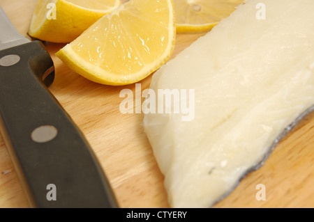 Filetto di eglefino e le fette di limone su un tagliere di legno Foto Stock
