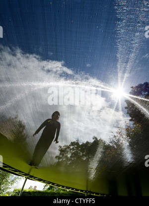 Grandangolo sparato contro il sole di una bambina su un trampolino, visto da sotto Foto Stock