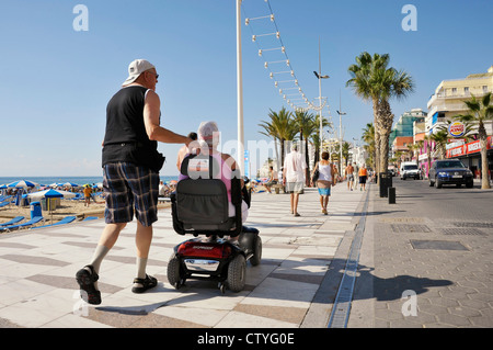 Accompagna l uomo donna su scooter elettrico sulla spiaggia di Levante lungomare di Benidorm, Spagna Foto Stock