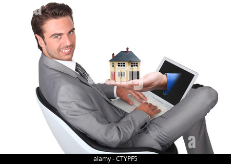 Giovane uomo in abito grigio seduta con laptop e incollaggio a mano fuori dello schermo Foto Stock