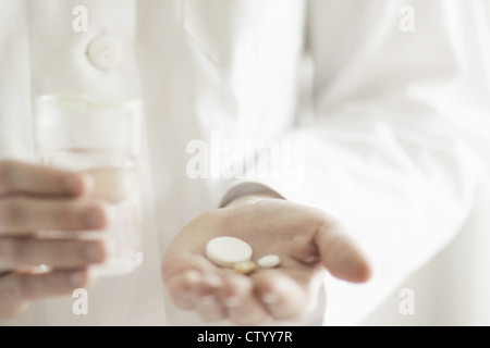 Medico azienda pillole con un bicchiere di acqua Foto Stock