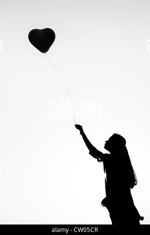 Indian ragazza adolescente tenendo un cuore a forma di palloncino. Silhouette. Monocromatico Foto Stock