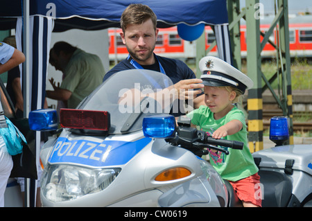 Piccola bionda Caucasian boy indossando una polizia berretto gode di cavalcare un tedesco della BMW pattuglia di polizia moto durante il public display Foto Stock