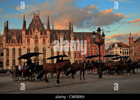 Il Palazzo del Governo è illuminata dalla luce della sera come carrozze trainate da cavalli attendere per turisti in Bruges, Belgio Foto Stock
