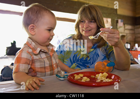 Nonna alimentare 13 Mesi nipote mentre è seduto al tavolo da picnic al mulino di primavera del parco statale in Indiana Foto Stock