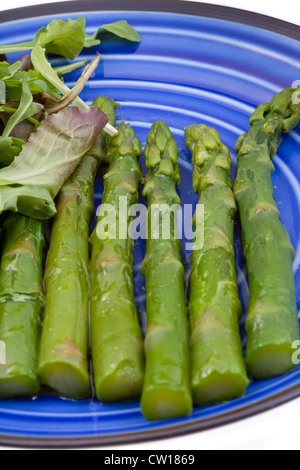 Bollito di asparagi verdi con insalata mix su piastra blu Foto Stock