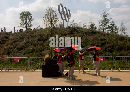 Giochi Maker volontari stessi ombra da un sole caldo sotto giganteschi anelli olimpici utilizzata come sfondo per gli spettatori" le foto durante il London 2012 Olympic Park. I volontari sono chiamati 'Giochi Makers', come stanno contribuendo a rendere i giochi accadere. Fino a 70.000 giochi politici prendere su di una ampia varietà di ruoli attraverso le sedi: da accogliere i visitatori, per il trasporto di atleti; ad aiutare dietro le quinte nella tecnologia team per assicurarsi che i risultati visualizzare quanto più rapidamente e accuratamente possibile. (Più didascalie in Descrizione.). Foto Stock