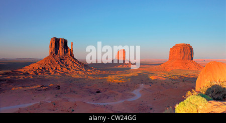 Vista panoramica di tre desert buttes dal punto di vista elevato al tramonto. Avvolgimento su strada sterrata, rocce in primo piano. Cielo senza nuvole Foto Stock