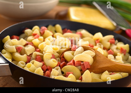 La preparazione di freschi fatti in casa il gomito maccheroni con salsiccia pezzi in padella con il formaggio e la cipolla verde nella parte posteriore Foto Stock