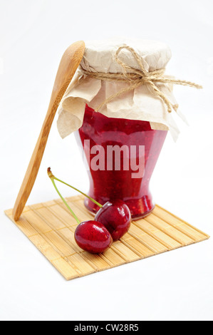 Vaso in casa di confettura di ciliegie e un paio di ciliegie con il cucchiaio di legno e coaster Foto Stock