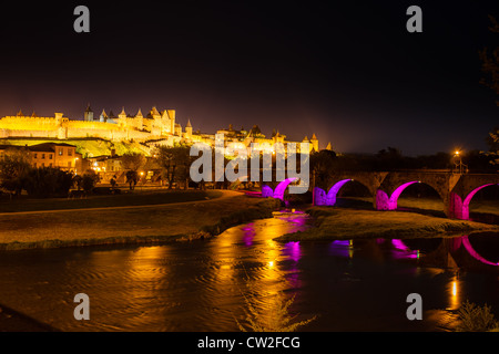 Illuminata bastioni medievali di antica città fortificata di Carcassonne con rosa luminoso viola gli archi del Ponte in nero cielo notturno Foto Stock