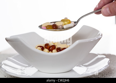 Cucchiaio di compresse di vitamina sospesa sopra il vaso di compresse per la colazione in cucina Foto Stock